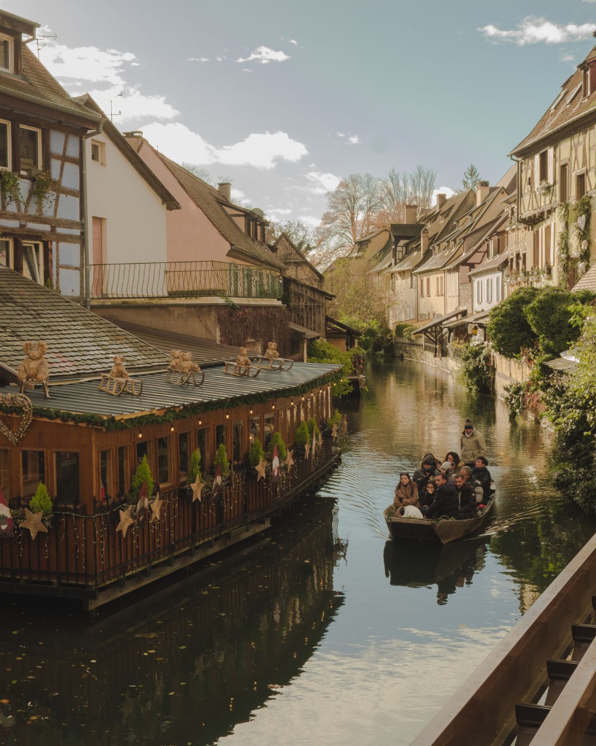 Picturesque village by the water, with charming pastel cottages and a small boat with people passing through.