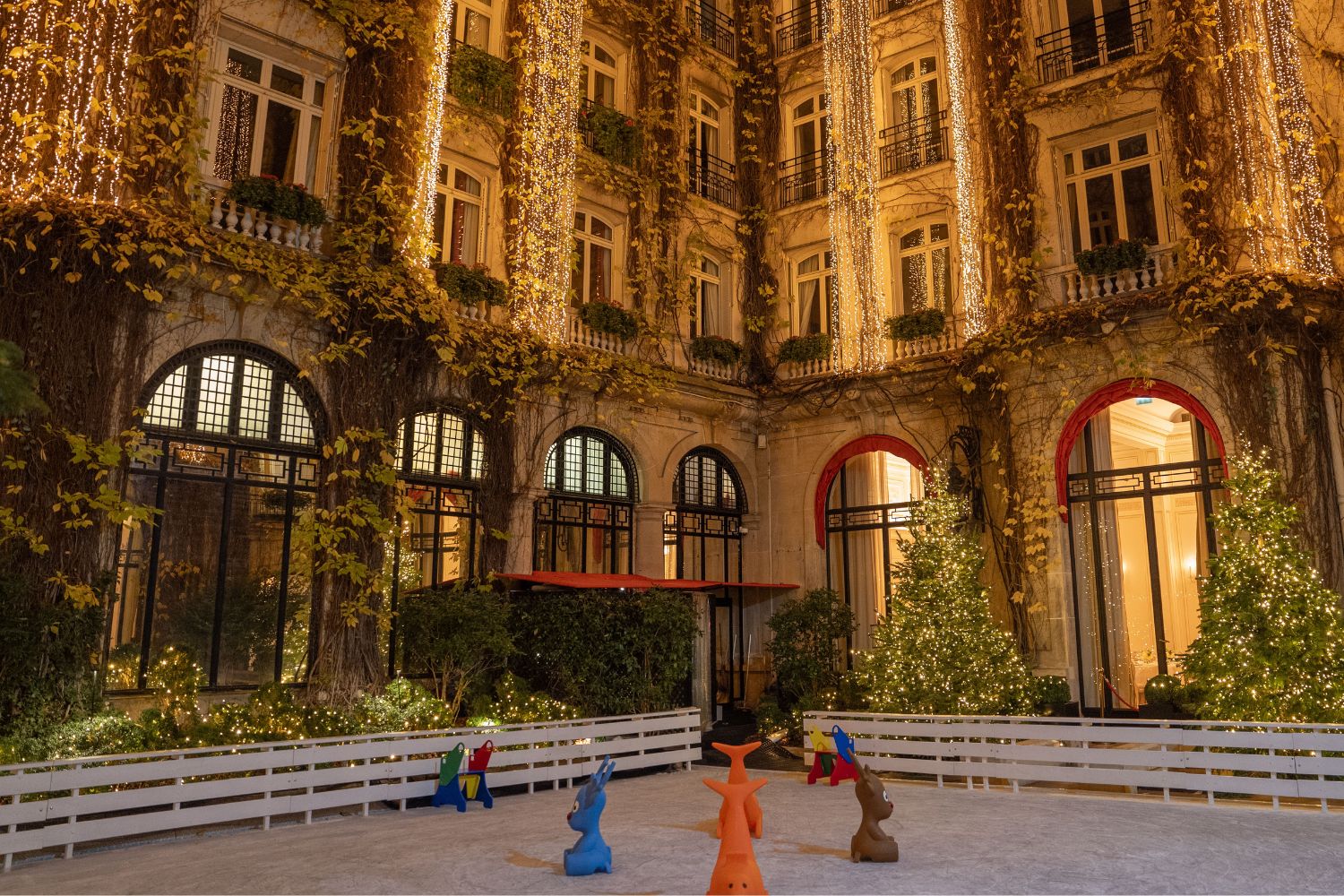 Ice skating ring in front of a highly ornamented building with Christmas lights.