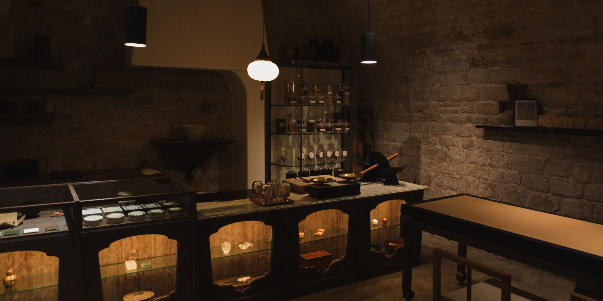 A tea store interior with stone walls, a wood table and counter, with glass shelves and glass pots in the back.