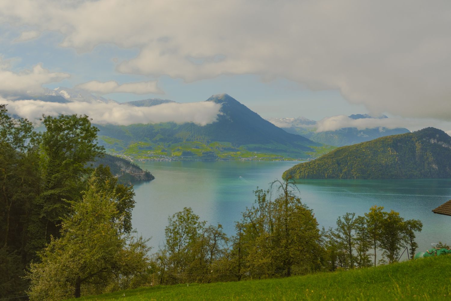Turquoise lake amidst dark green mountains and white clouds.