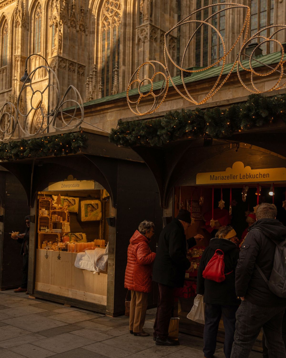 A Christmas market setting, in front of a cathedral façade, with dark wooden stands.
