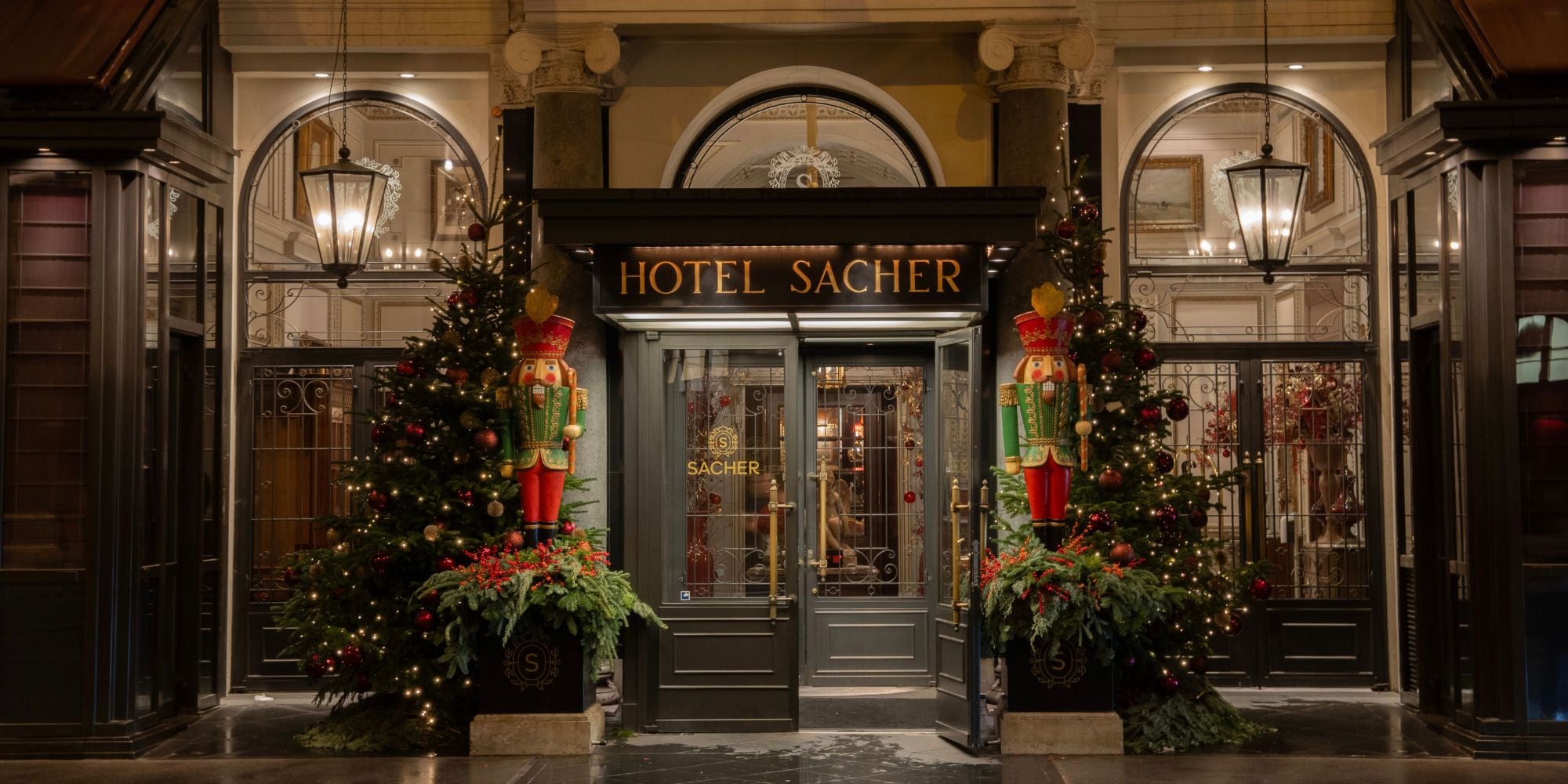 A classic hotel façade with a dark grey entrance door, Christmas ornaments on the side at nighttime.