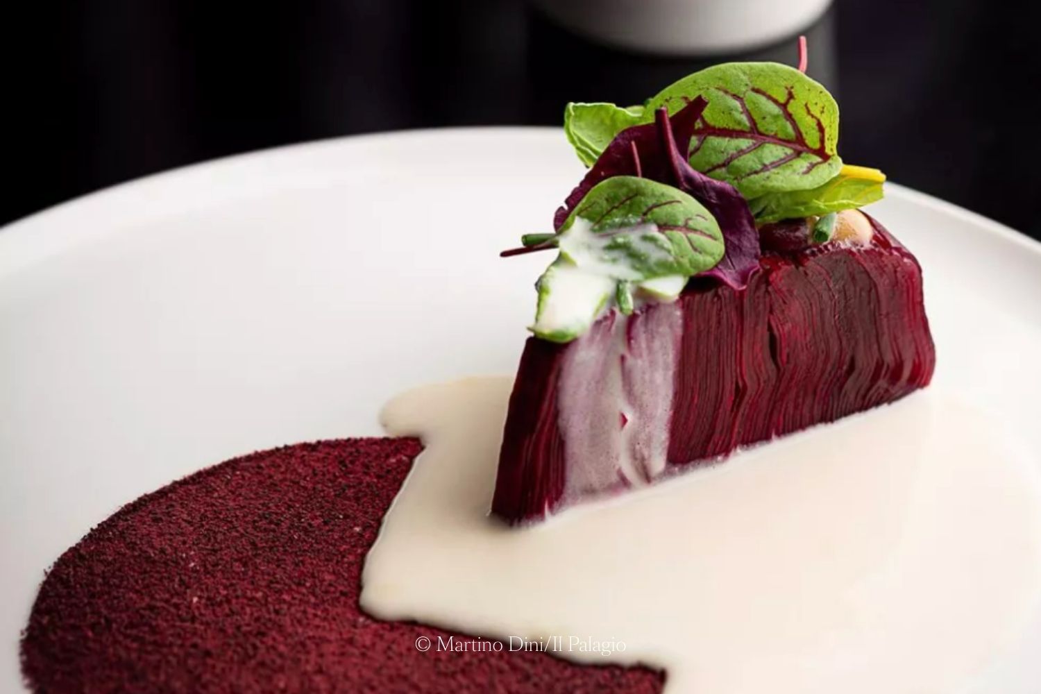 Magenta slice white aromatic herbs on top, a cream sauce and a magenta base on a white dish.