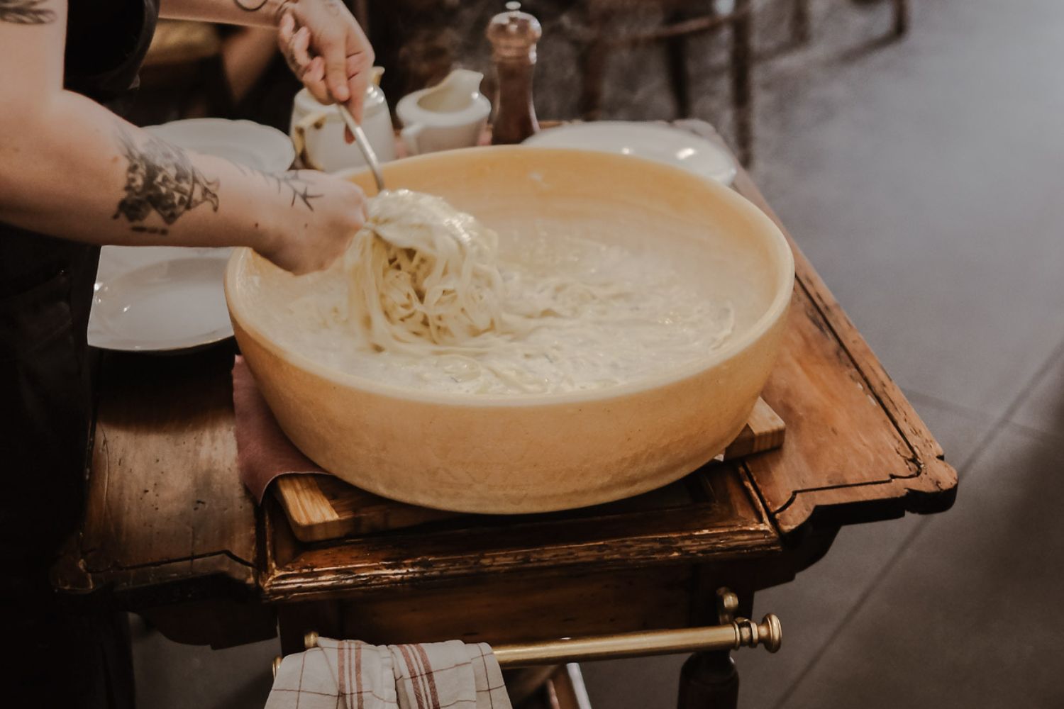 Pasta dipped into a large melting cheese, over a rustic wooden table.