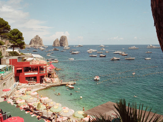 Marina Piccola beach, full with colourful umbrellas, and the Faraglioni in the distance, in Capri