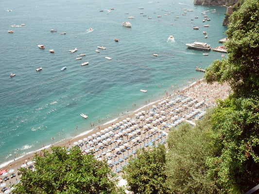 Positano beach full of umbrellas and people, and the yachts in the bay, in the Amalfi Coast