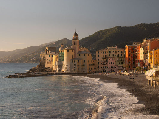 The beach and church of Camogli, near Portofino, in the late afternoon, as the soft, low sunlight creates a beautiful contrast of colour and shadows on the buildings façades and the hillsides in the distance. 
