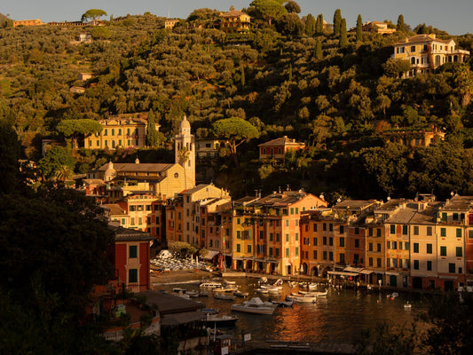 The village of Portofino, with its colourful pastel-toned buildings around the harbour, where a few fishing boats float in the quiet waters, under the golden morning light.