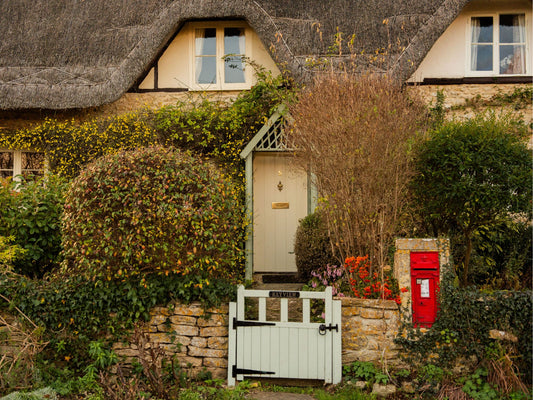 Thatched roof cottage in Lacock, Cotswolds, with a white gate and red postbox.