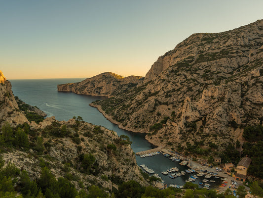 The Calanque Morgiou, surrounded by white limestone cliffs covered in pines, during sunset hours