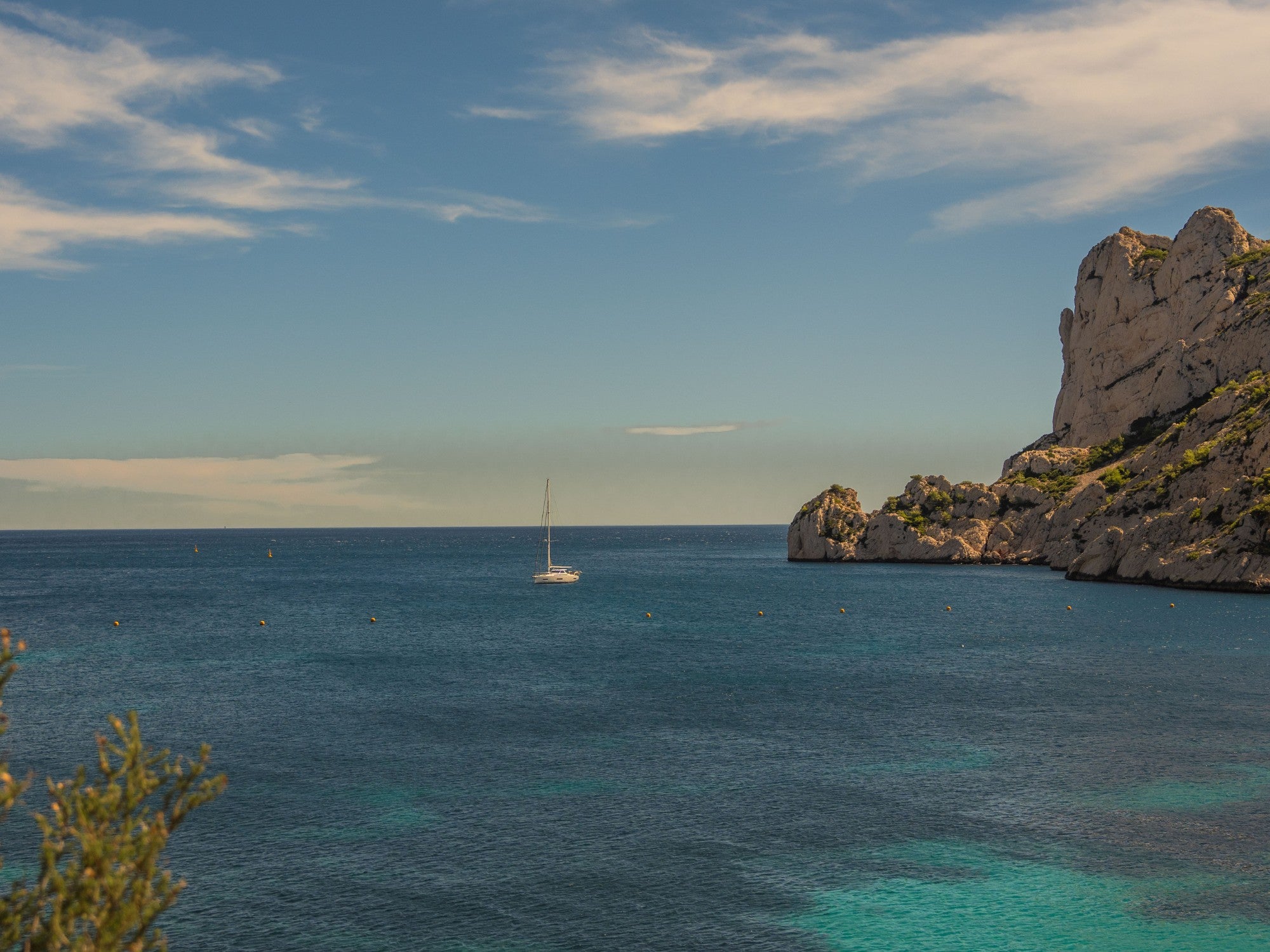 A lonely sailboat in the calm azure waters of the Mediterranean surrounded by white limestone cliffs in the Parc National des Calanques in Marseille