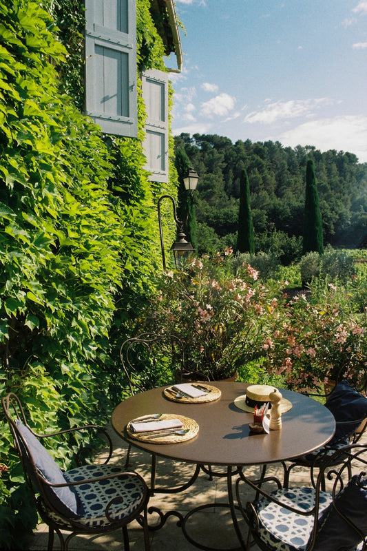 A table set for breakfast amidst a very lush Provençal garden, with ivies and cypresses, on a Summer morning