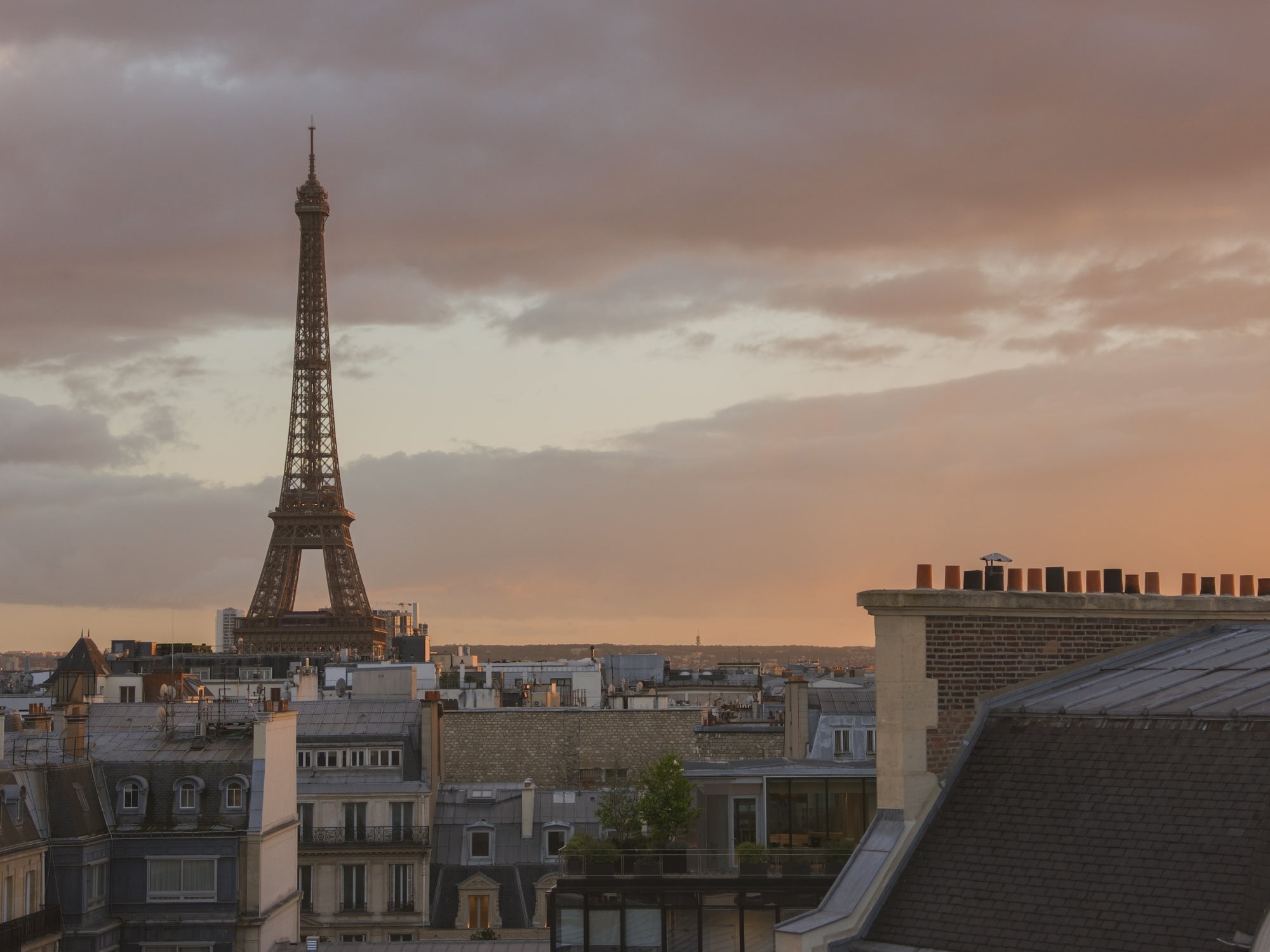 Views of the Eiffel Tower at sunset with a golden sky and the Parisian roofs