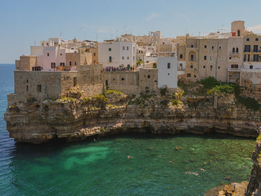 The town of Polignano a Mare built on the clifftops overlooking the people swimming in the turquoise water bay