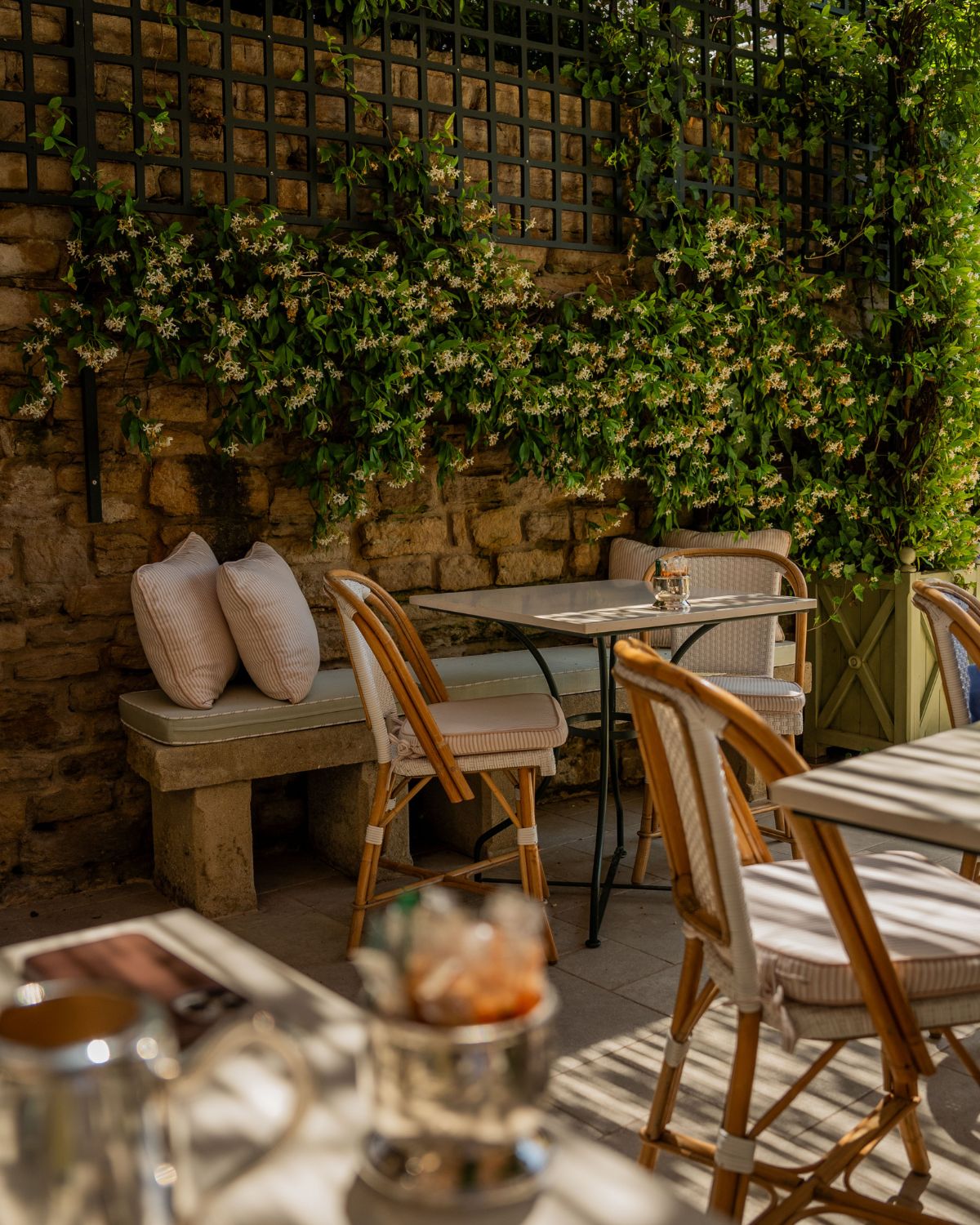 Secluded outdoor coffee space with wooden chairs, striped pillows, and climbing flowers.