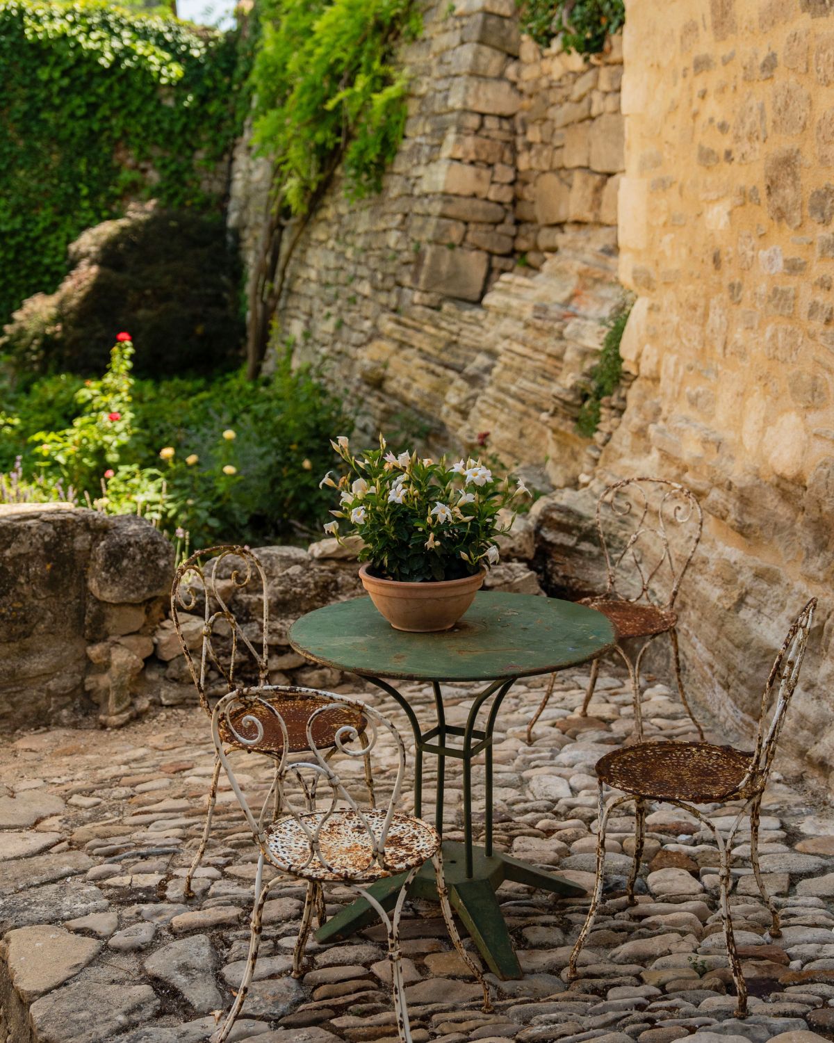 Cobblestone street in Lacoste with iron furniture, greenery and a vase.
