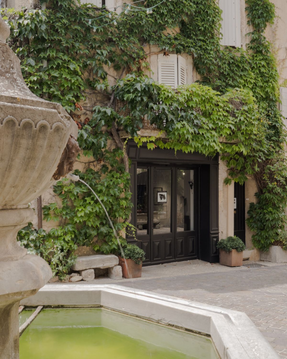 Charming fountain in Venasque. Shuttered windows, cobblestone streets, soft pastel tones and climbing plants.