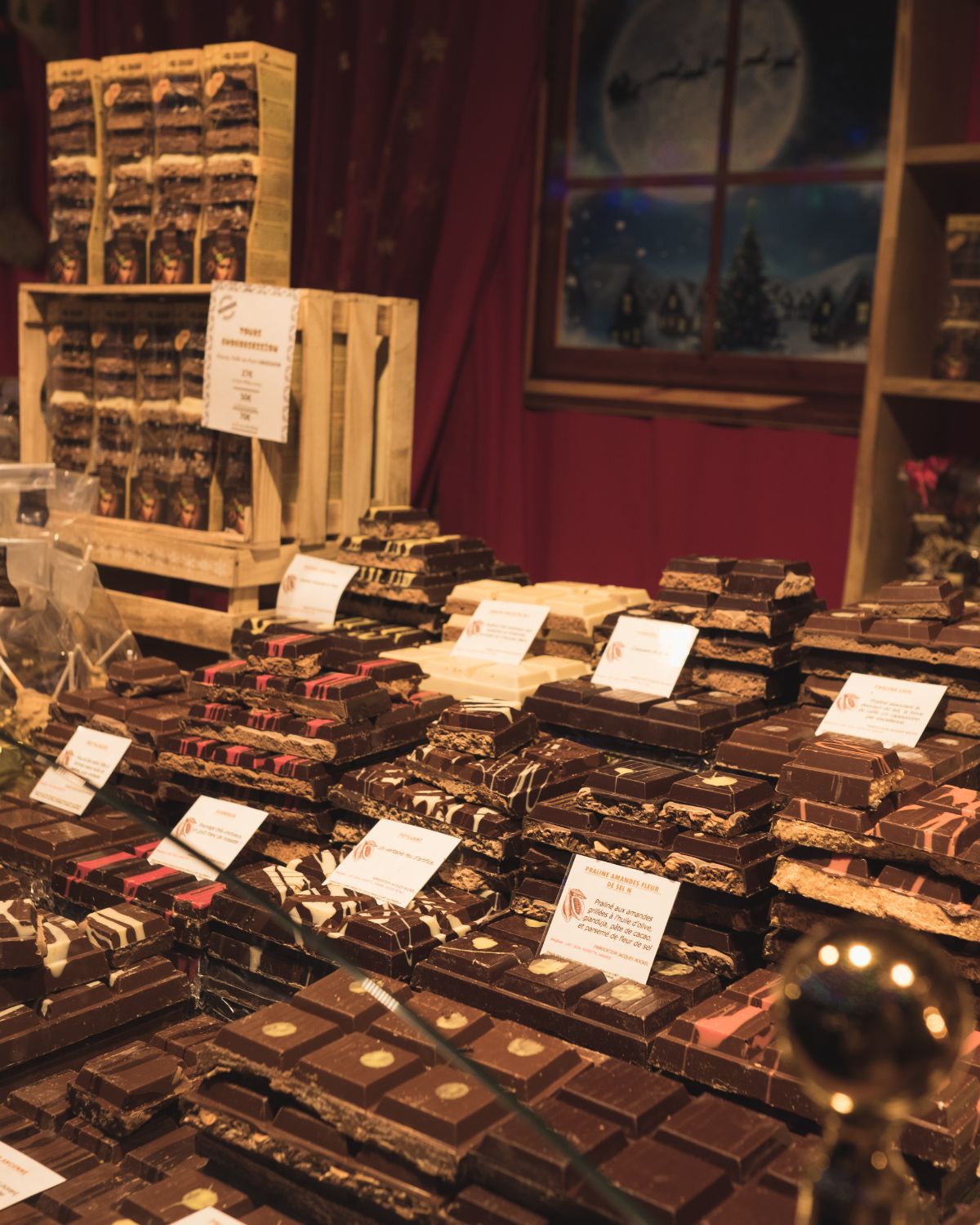 Chocolate boards of different kinds, placed on a stand, behind a glass divider at a Christmas market.