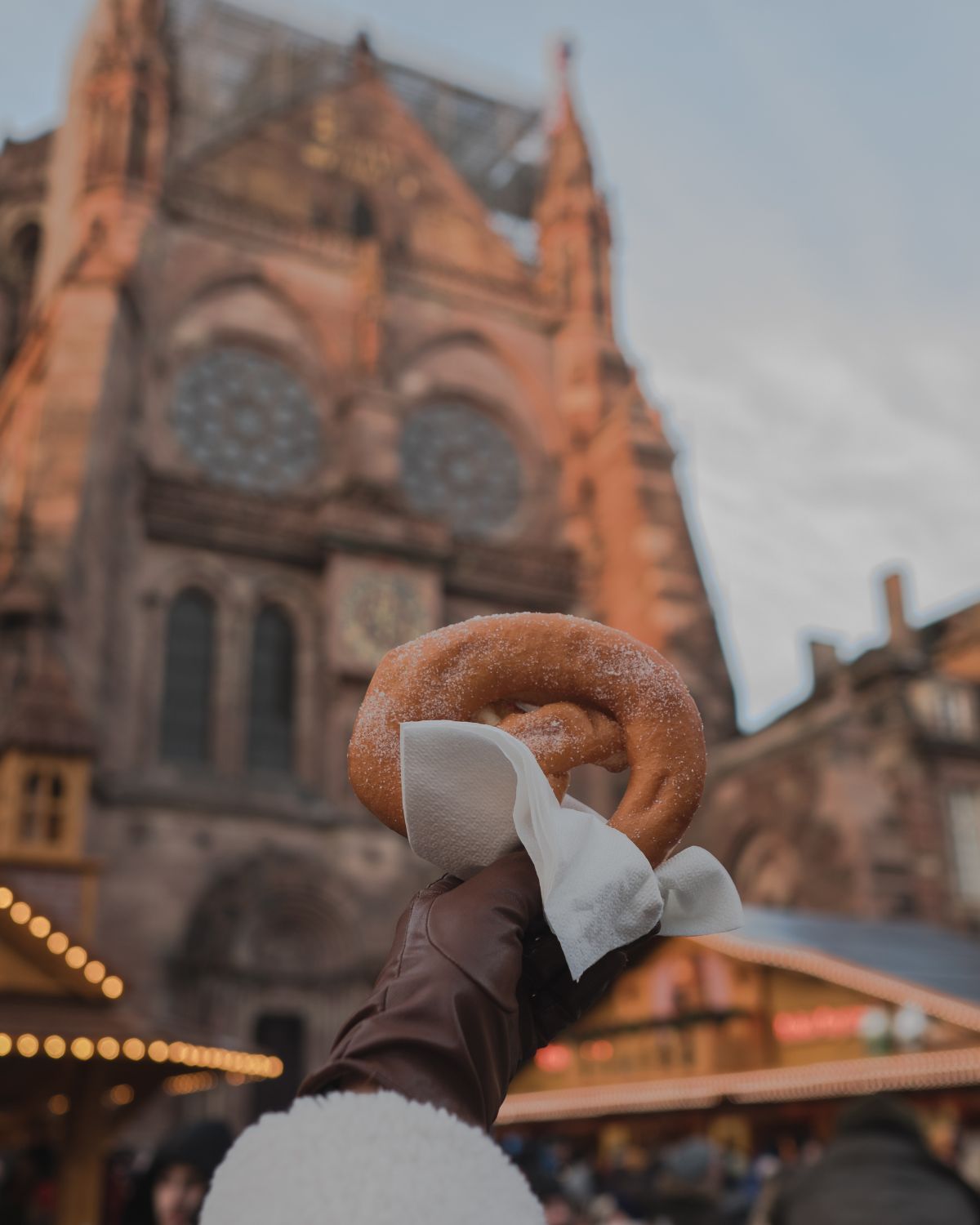 A hand with a brown glove holding a sweet in front of the Strasbourg Cathedral.