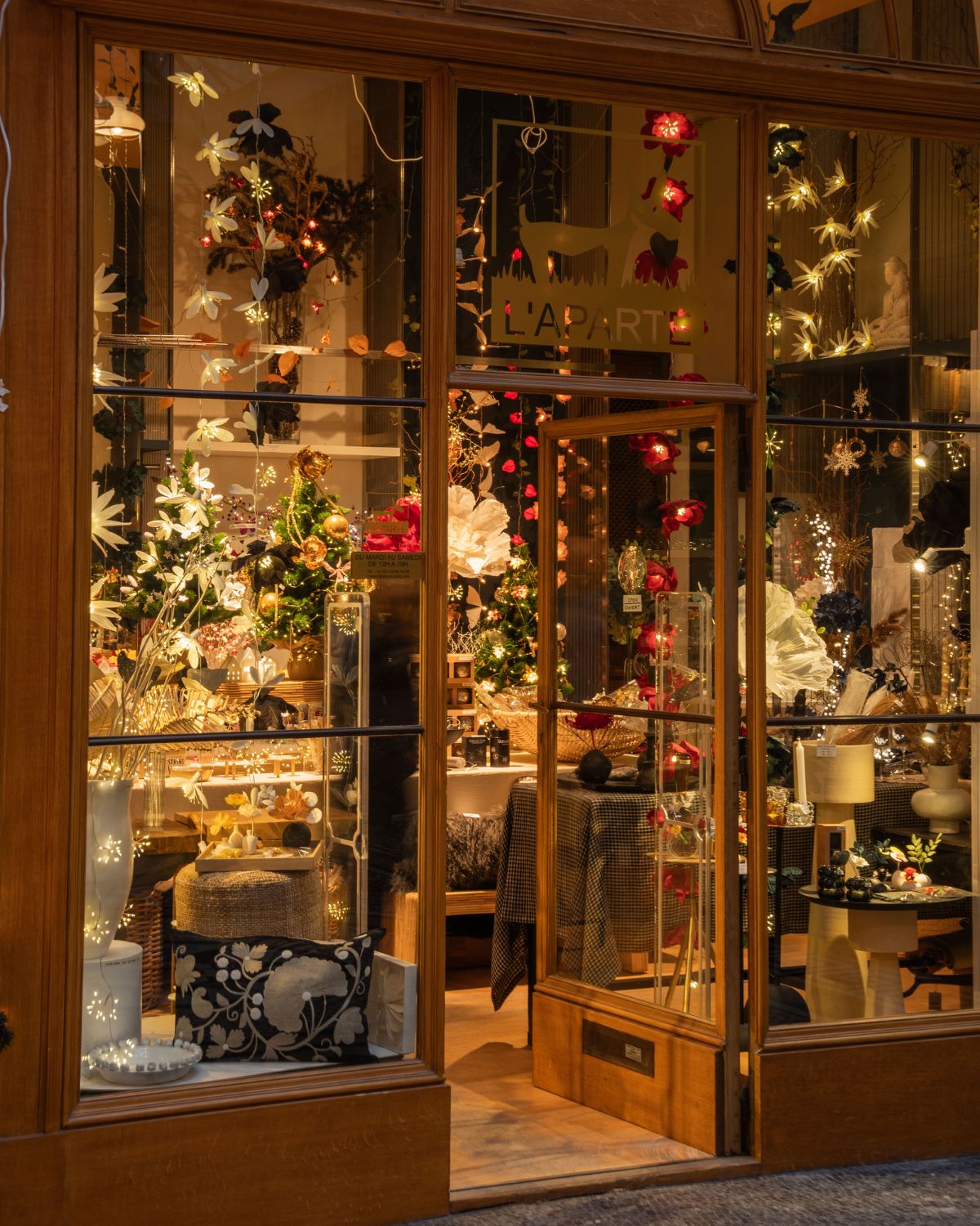 A store entrance, with glass and wooden windows, adorned with Christmas ornaments and lights on the inside.