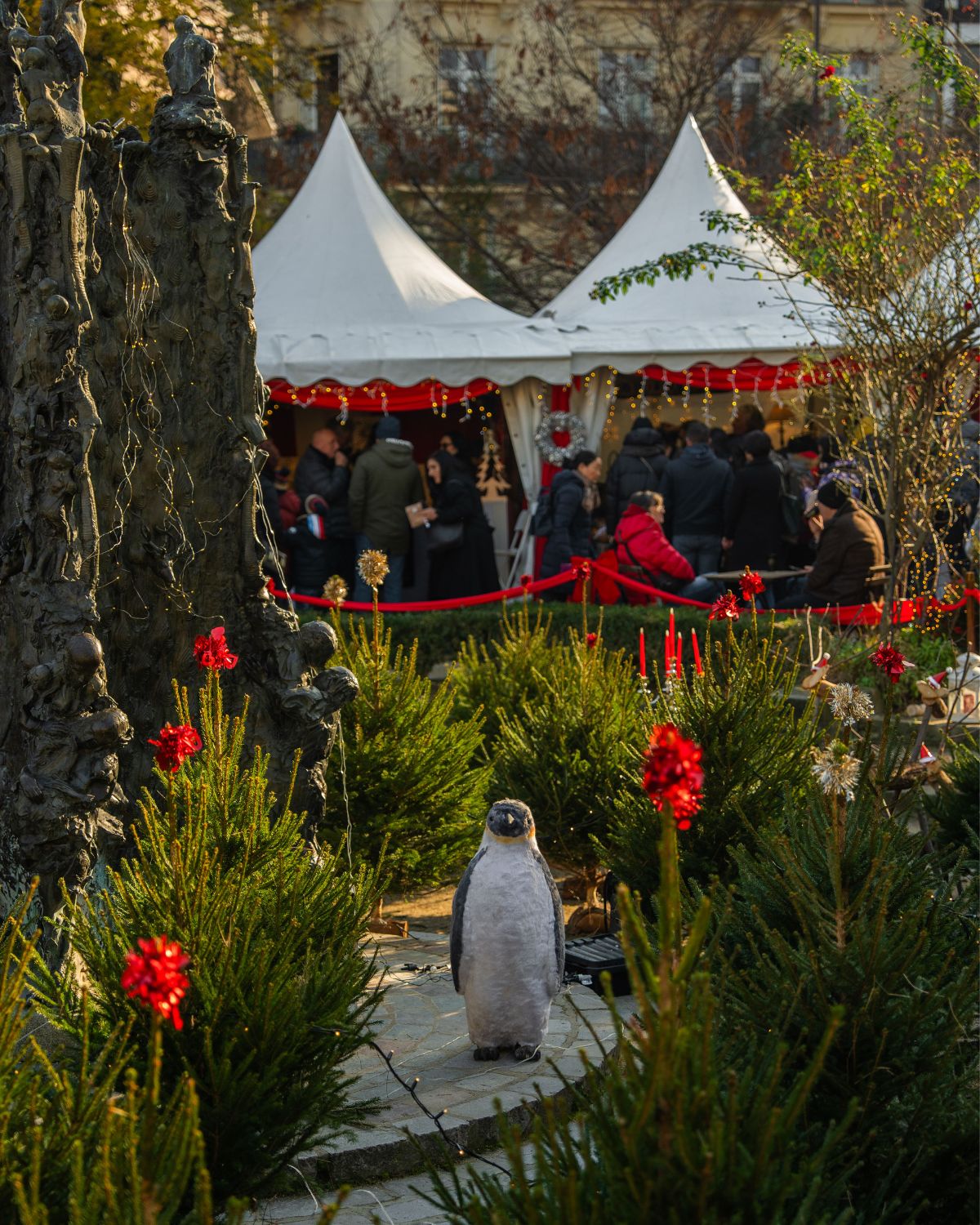 Christmas market outdoor setting, in a garden, with a pingiun in the center and white tends in the background.