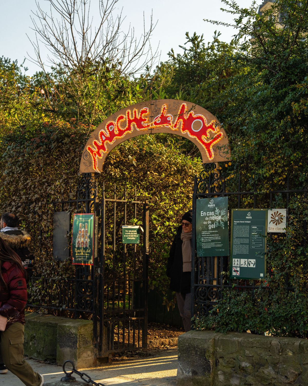 Christmas market entrance, with an archway and lights, in the middle of a garden's bushes.