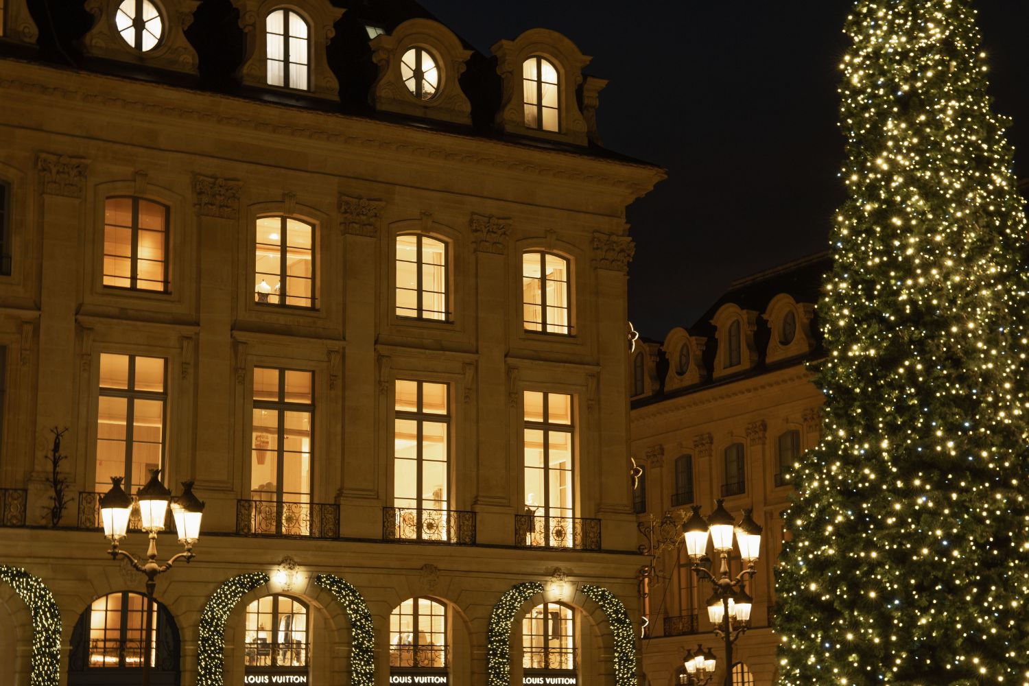 Christmas tree with lights, in front of a classic building in Paris, with ornaments adorning the windows and doors of the building.