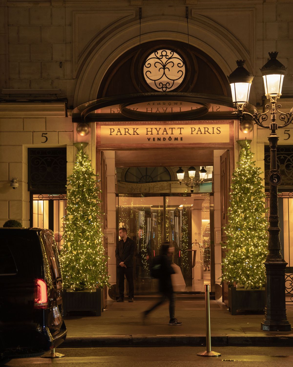 Hotel entrance door, on a classic building, with an antique outdoor high black lamp and two Christmas trees light lights by the side.