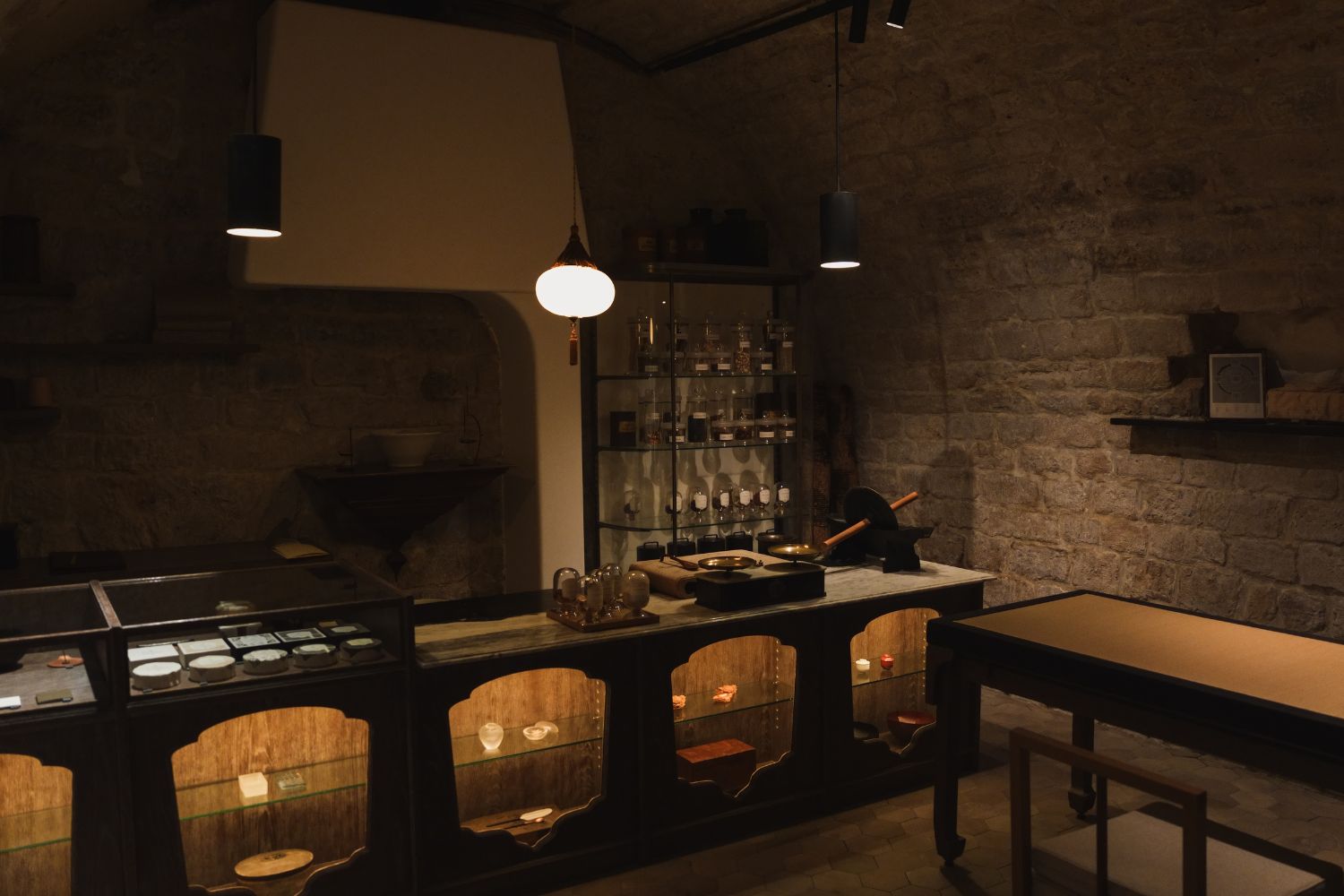 A tea store interior with stone walls, a wood table and counter, with glass shelves and glass pots in the back.