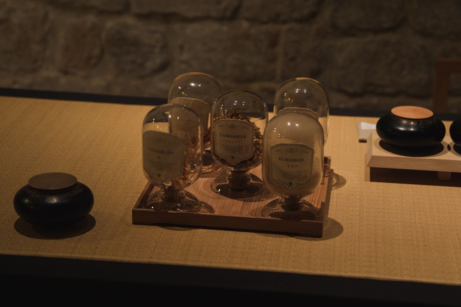 Glass pots with infusions, on top of a table facing a stone wall.