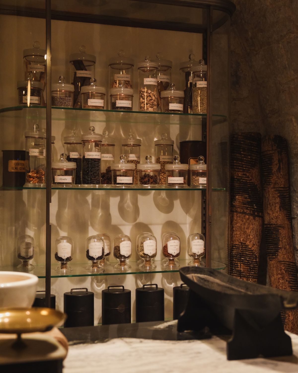 Glass pots with infusions on glass shelves, next to a stone wall.