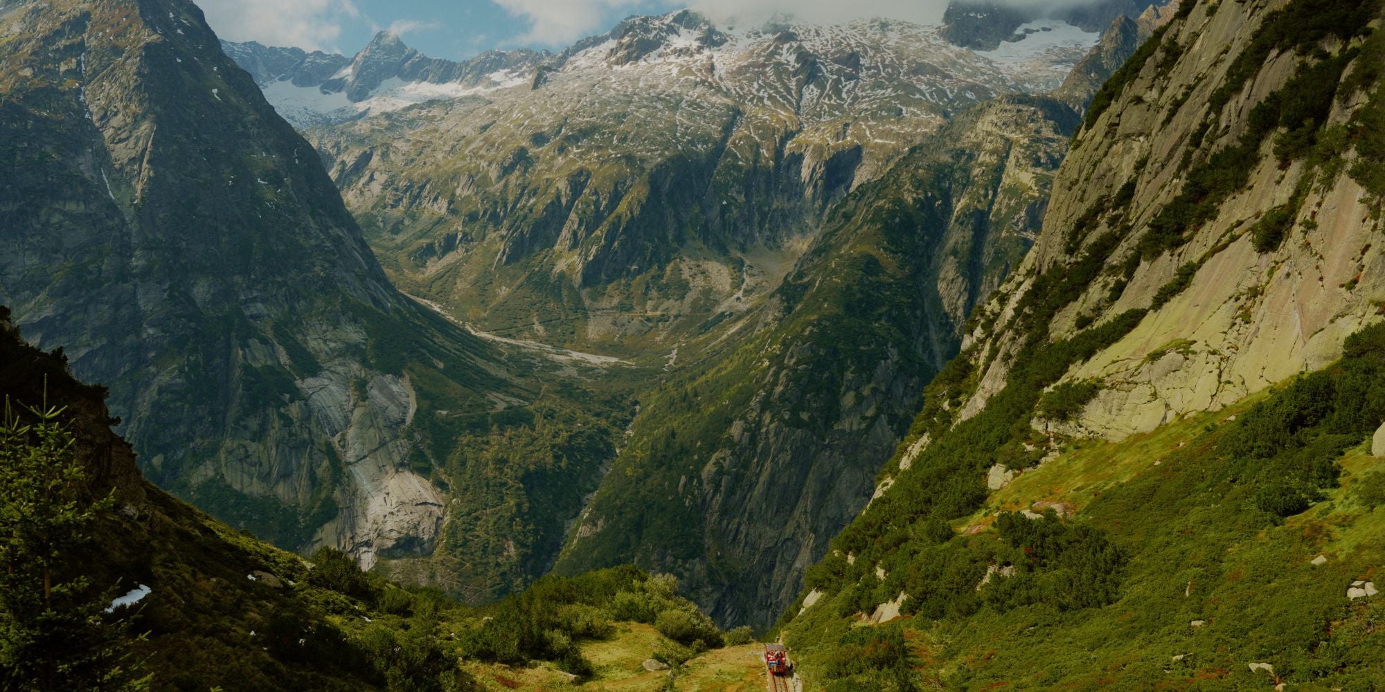 Green luscious mountains, with partial snow in the background and a re train slide.