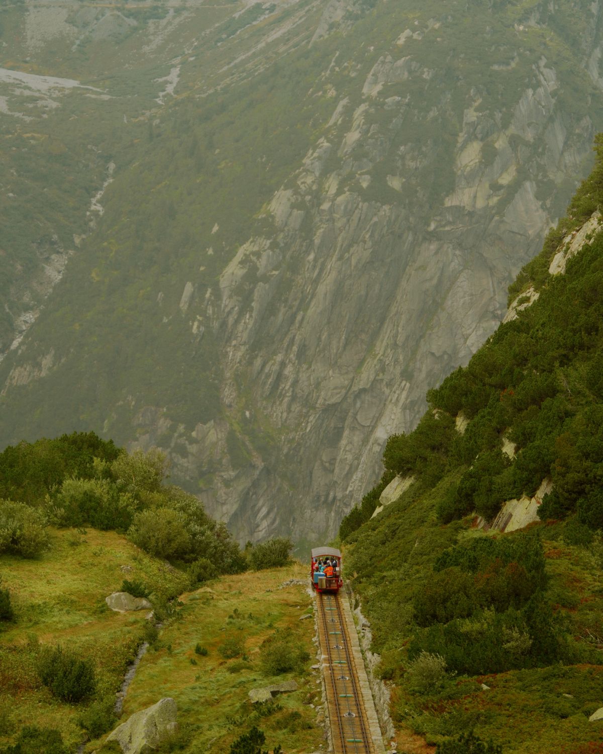 Red train on trails, amidst green mountains.