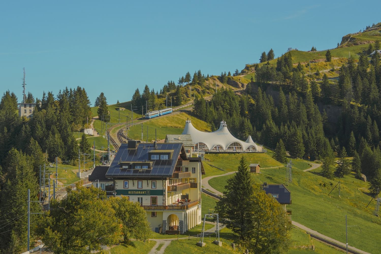Mountain hilltop with houses, train rails and high trees.