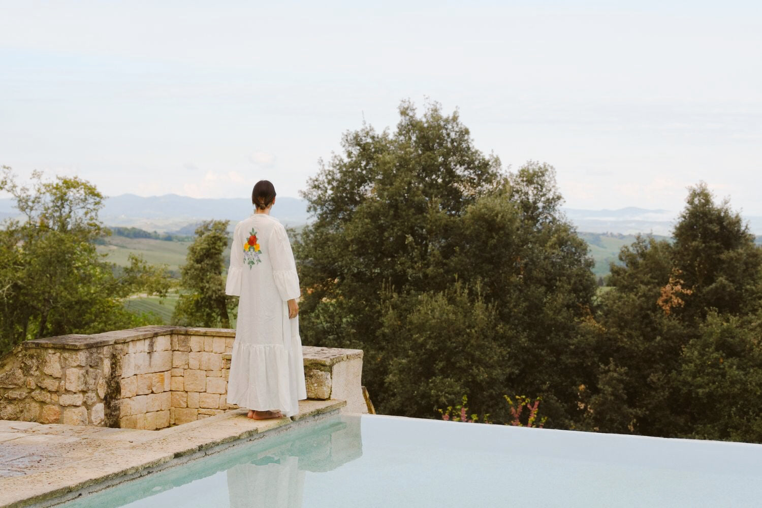 Lady in a white dress next to a pool, overlooking the Tuscan hills.