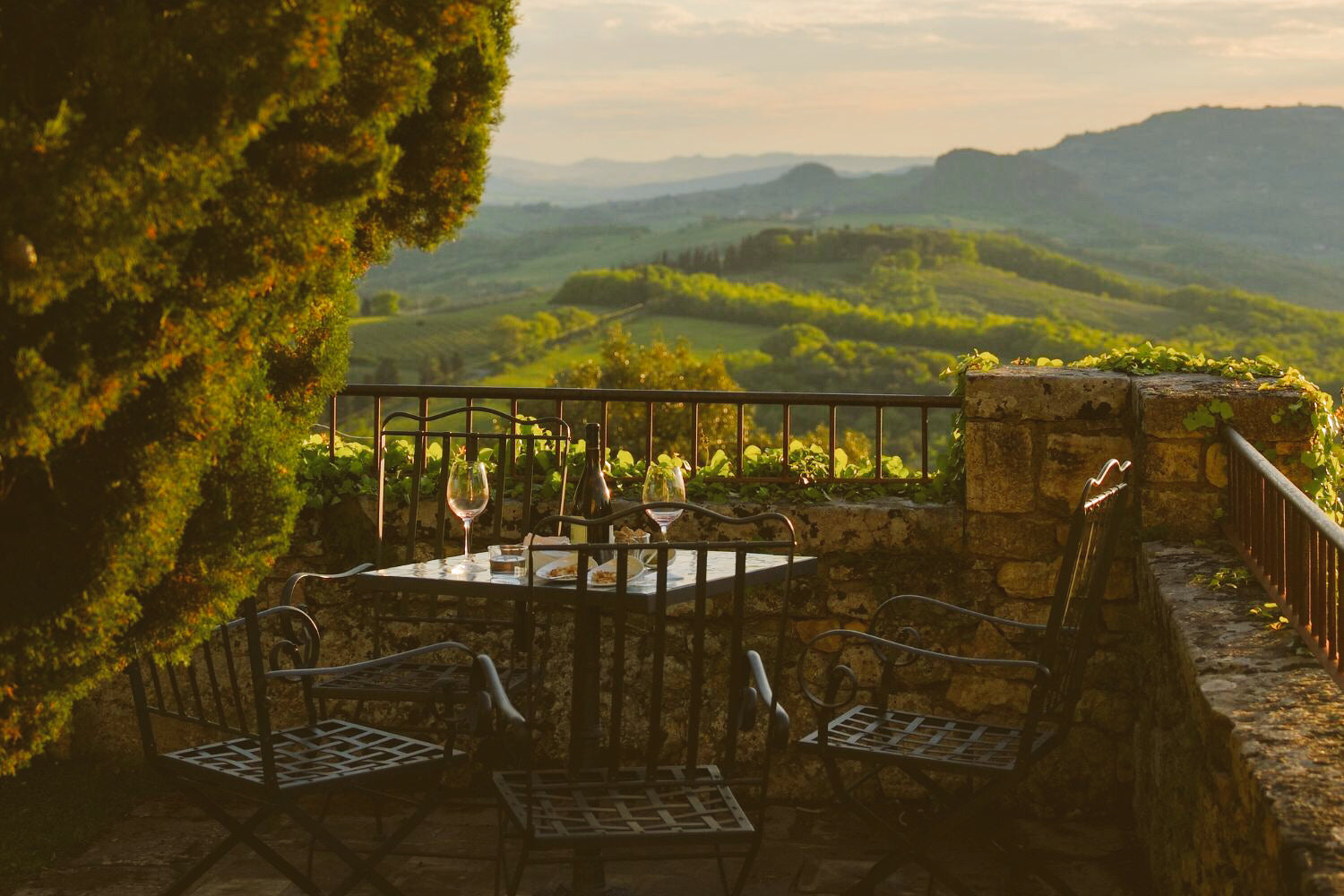 Picturesque balcony with iron outdoor chairs and a table, facing the green Tuscan hills.
