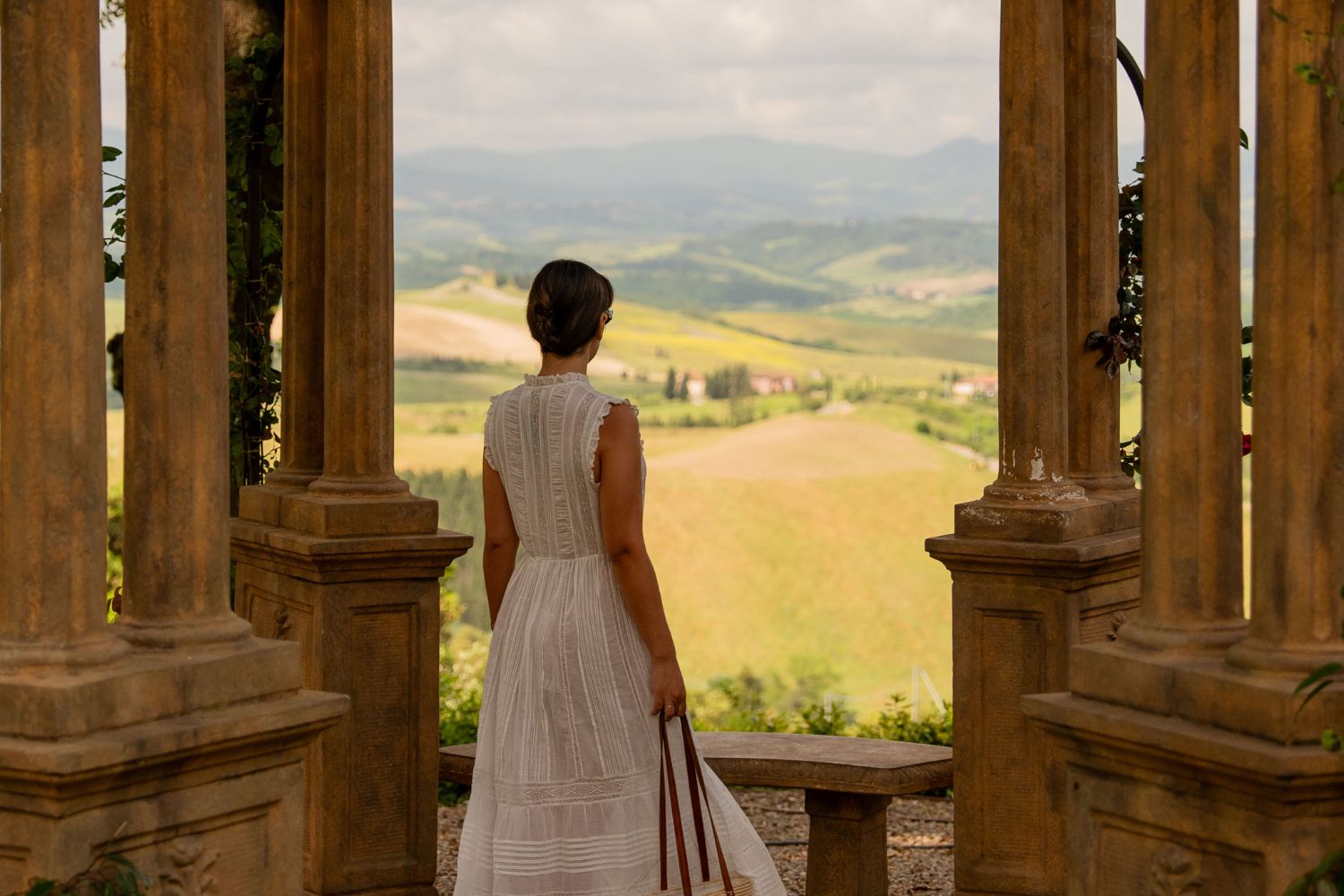 Young lady with a white dress, overlooking the green Tuscan hills.