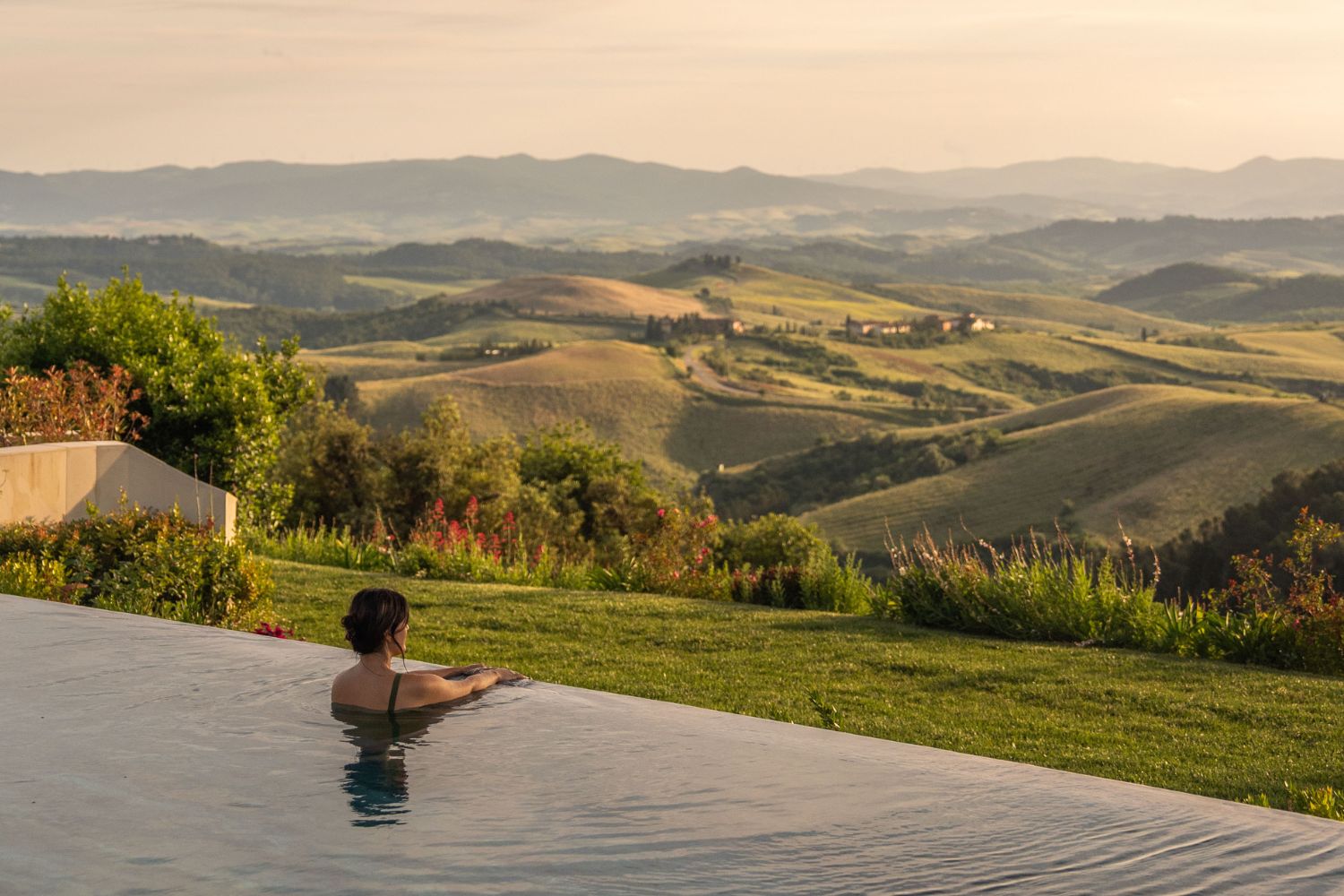 A young lady in an infinity pool, facing the green hills of Tuscany.