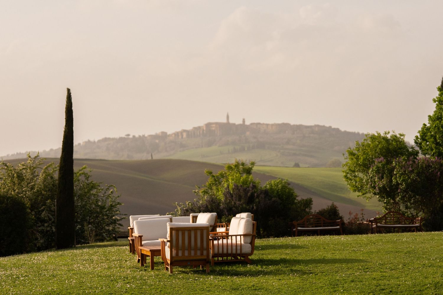 White and wooden outdoor seating, facing the hills of Tuscany and a picturesque village in the back.
