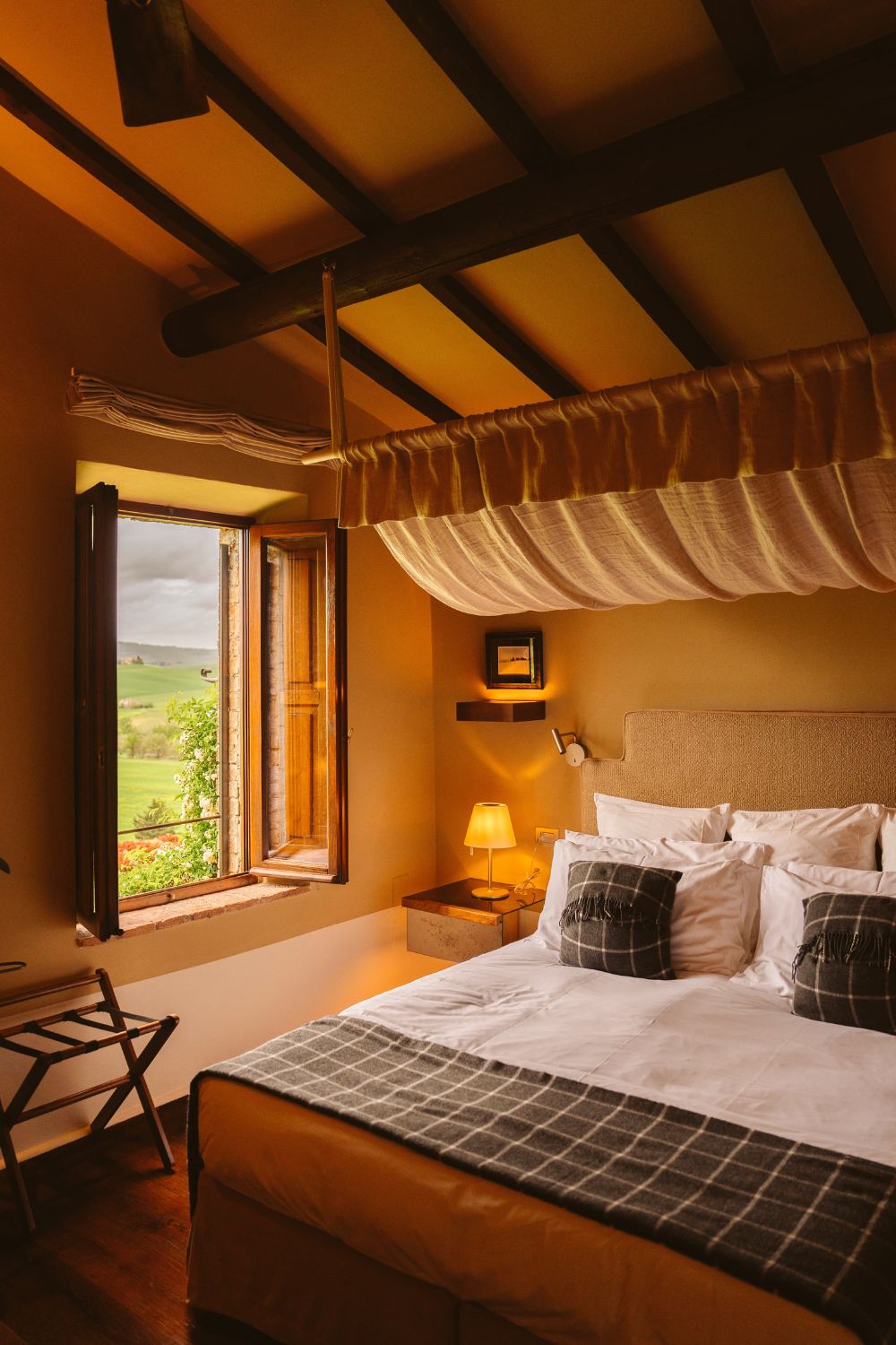 A warm toned hotel bedroom, with wooden beams, white and dark green bedding.
