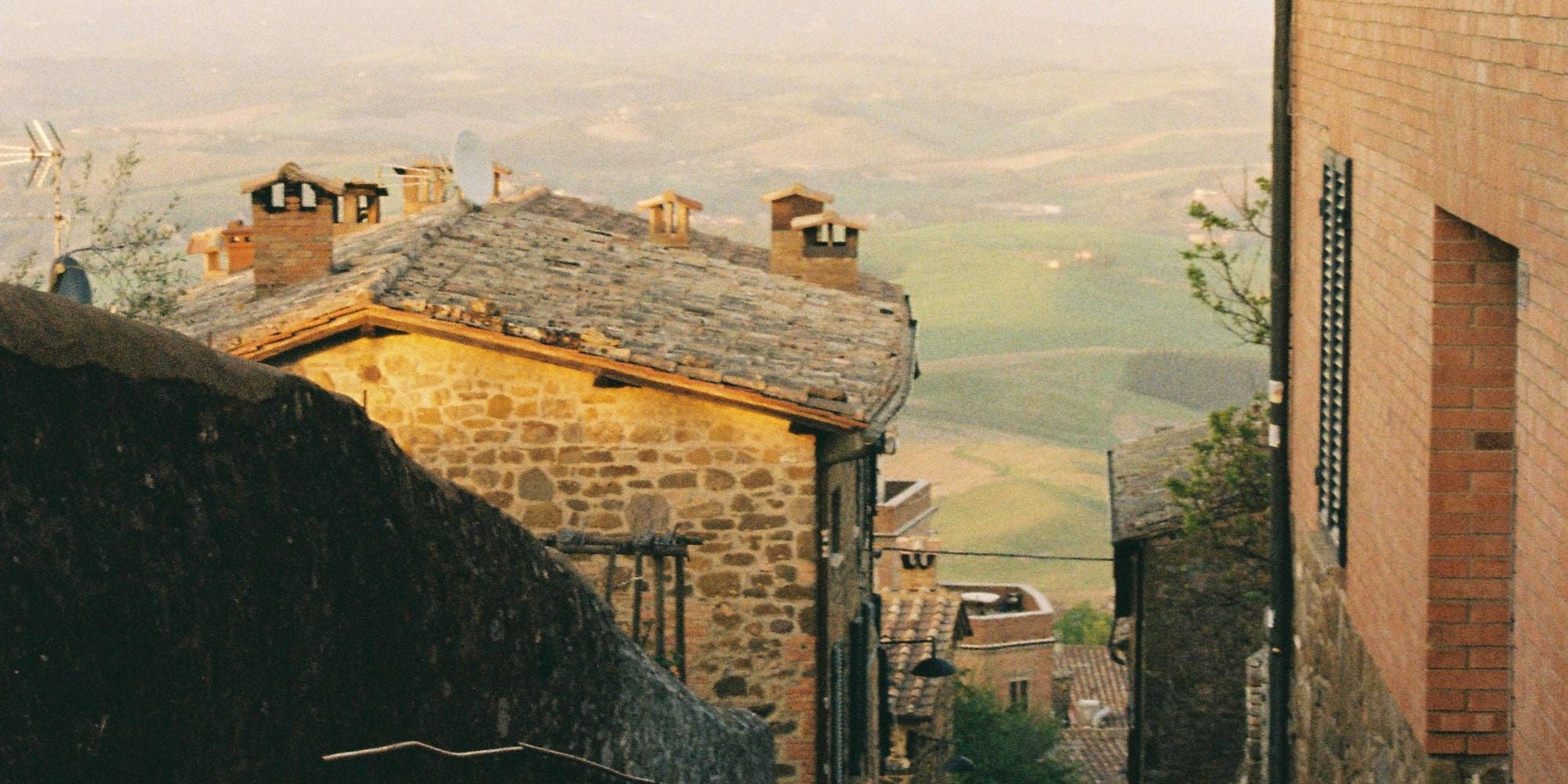 Cobbled stone houses, sitting on a hill, with valleys in the background and a golden light shimmering.