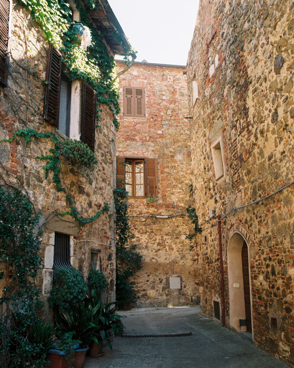 Streets with cobbled stone houses, shuttered windows and several vases with plants on the floor.
