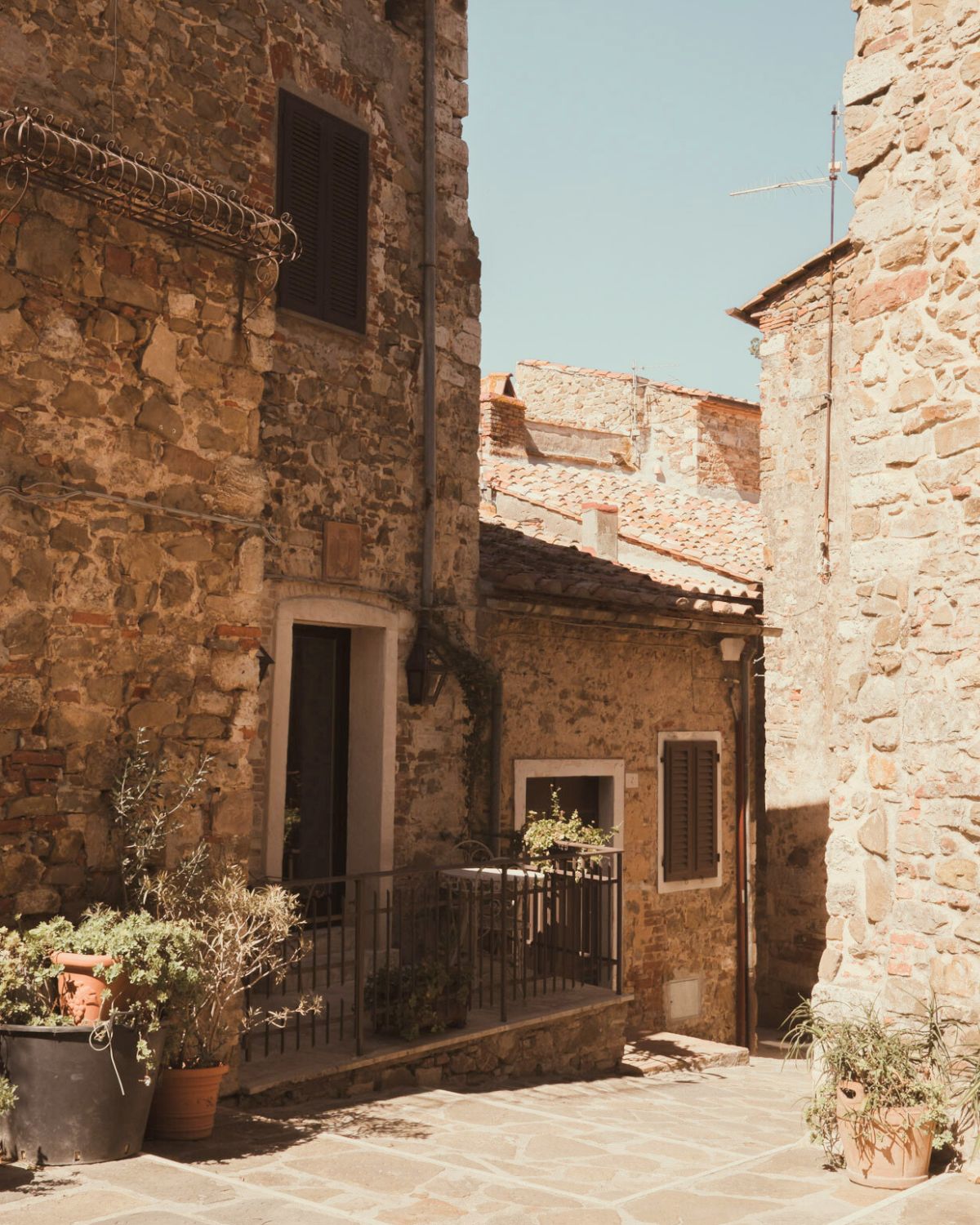Cobbled stone houses, with shuttered windows and several vases with plants on the floor.