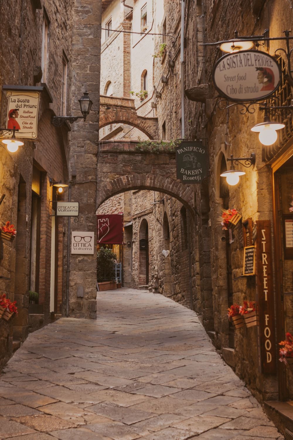 Street alley with several arches,with red flowers on the walls, cobbled stone façades and floor.