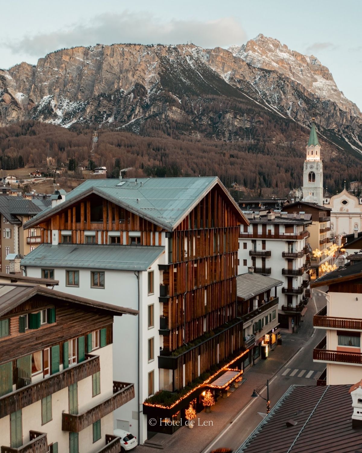 A small city with dark wood and white buildings, alpine style, and a snowy mountain in the back.