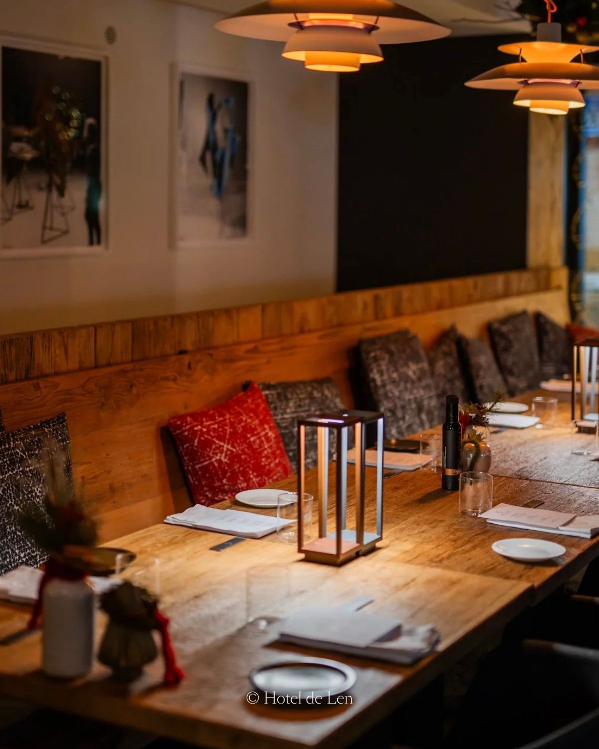 A restaurant setting with a warm wooden table and bench, and warm ceiling lights.