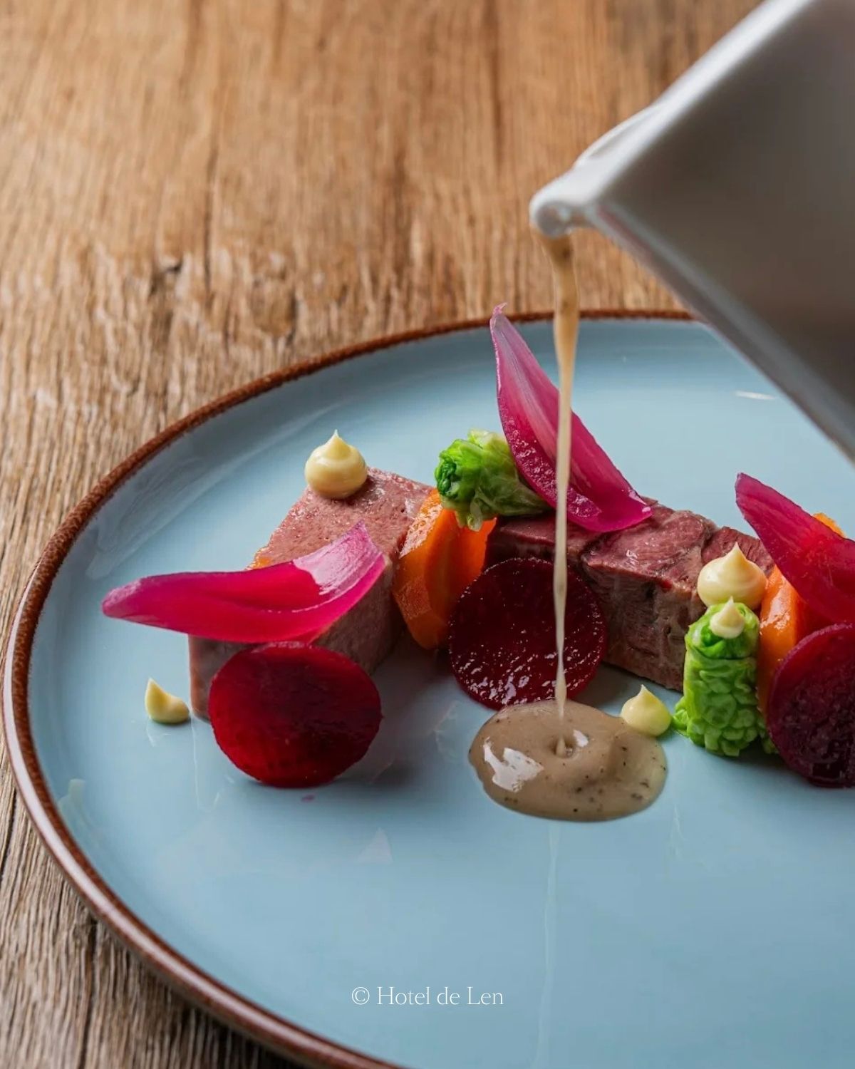 Fine dining course on a blue plate, over a wood table.