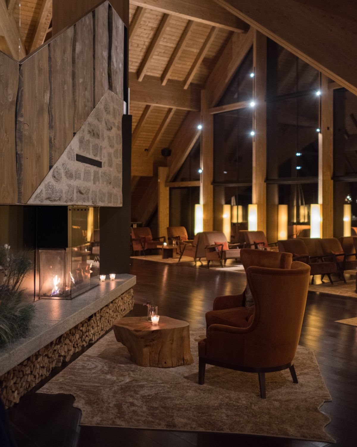 A wooden high cabin like living room at night, with brown and orange furniture and a fireplace.