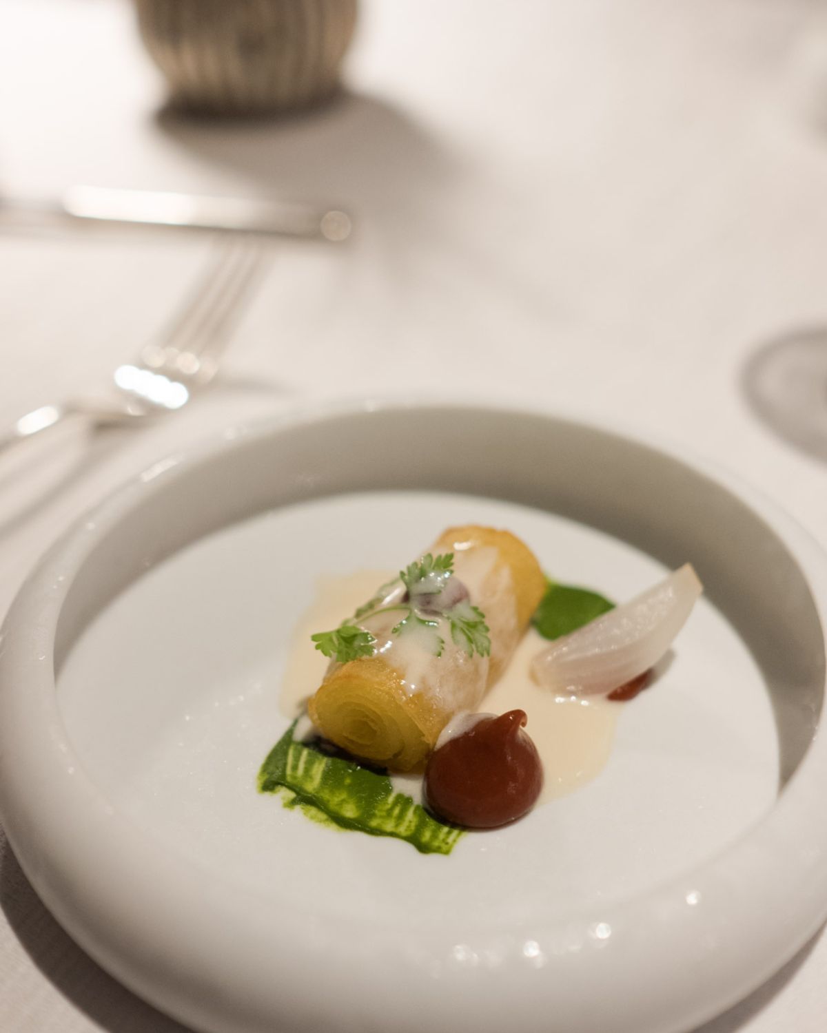 Fine dining course on a white plate and linen cloth.
