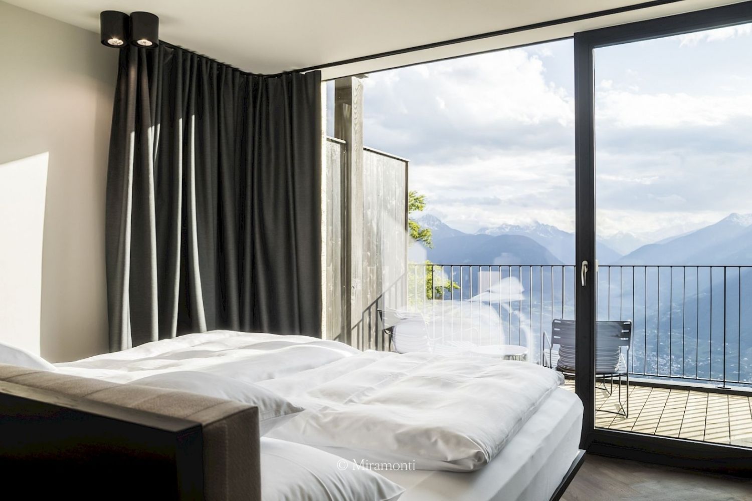 White and dark grey bedroom, with a balcony overlooking snowy mountains.